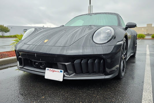 Front view of a black Porsche car with a California license plate on a wet road.